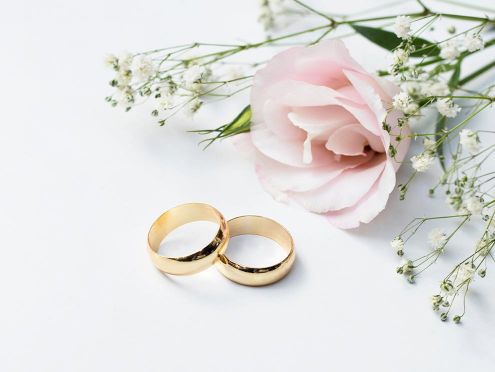 Golden wedding rings lying in front of a pink flower