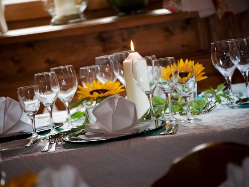A decorated dining table with sunflowers and wine glasses. In the foreground, a plate with a fanned-out napkin