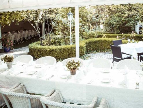 Festively decorated wedding table in the Limmerhof garden with white plates, cutlery and floral decorations.