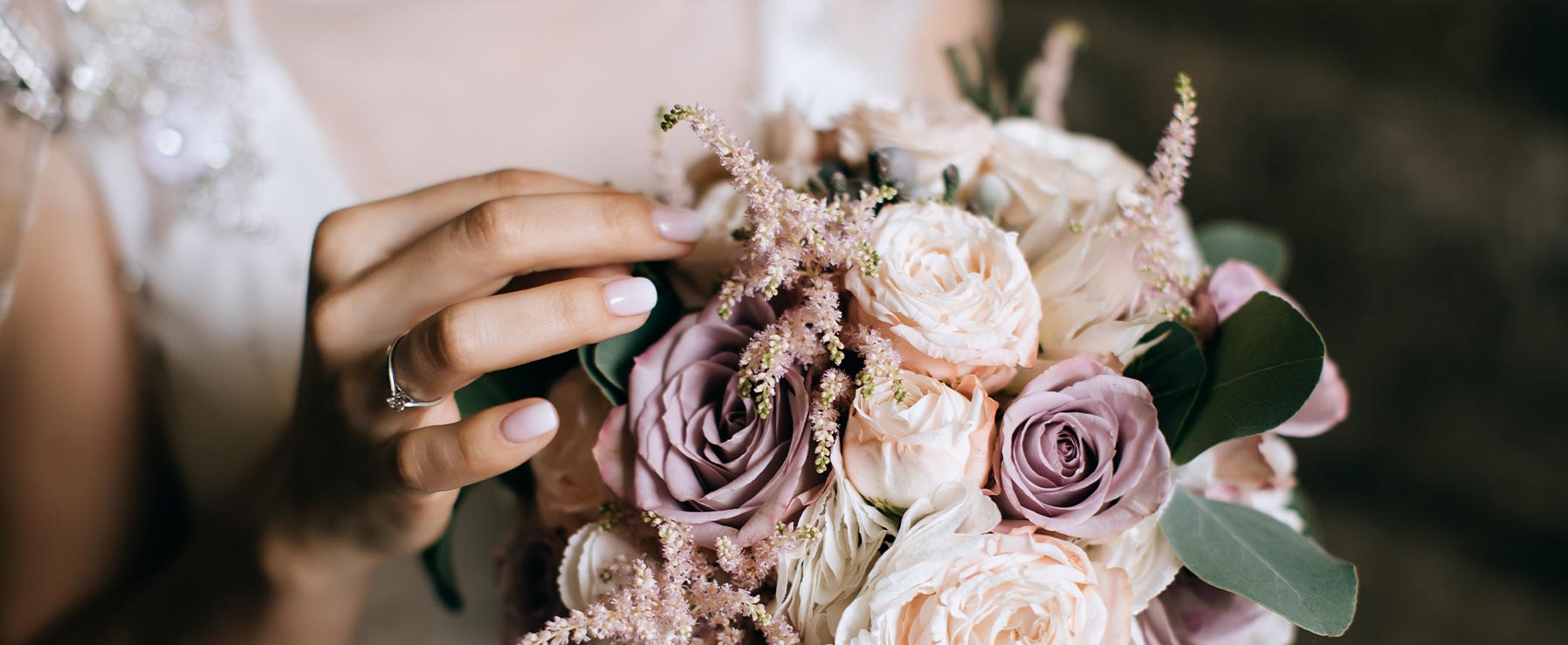 Detail of a bride in white with a wedding bouquet of white and purple roses in her hands.